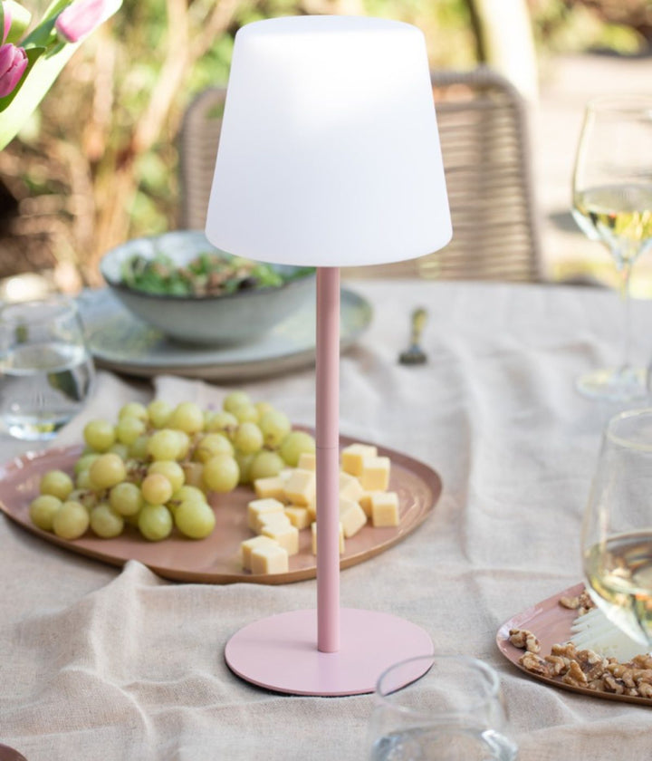 Lampada da tavolo Outdoors rosa su tavolo da giardino apparecchiato con uva e formaggio.