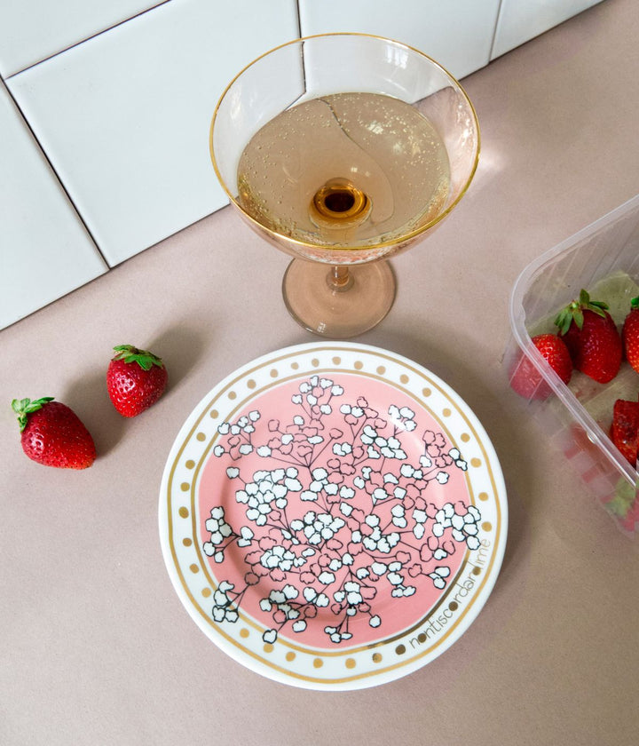 Tavola apparecchiata per aperitivo con champagne e fragole e piatto in porcellana decorato con la scritta non ti scordar di me