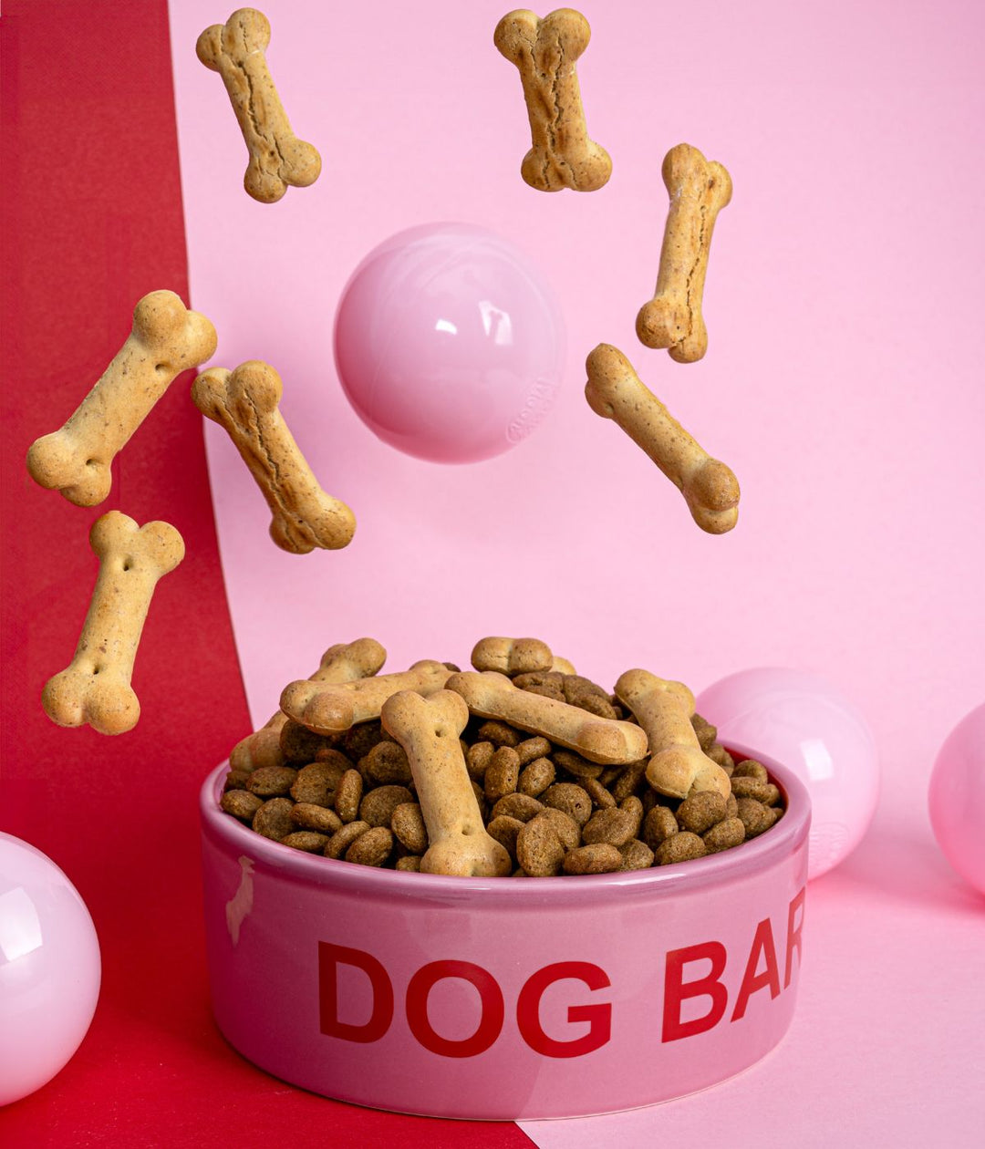 Ciotola Dog Bar rosa piena di croccantini e ossi per cani, con sfondo decorativo.