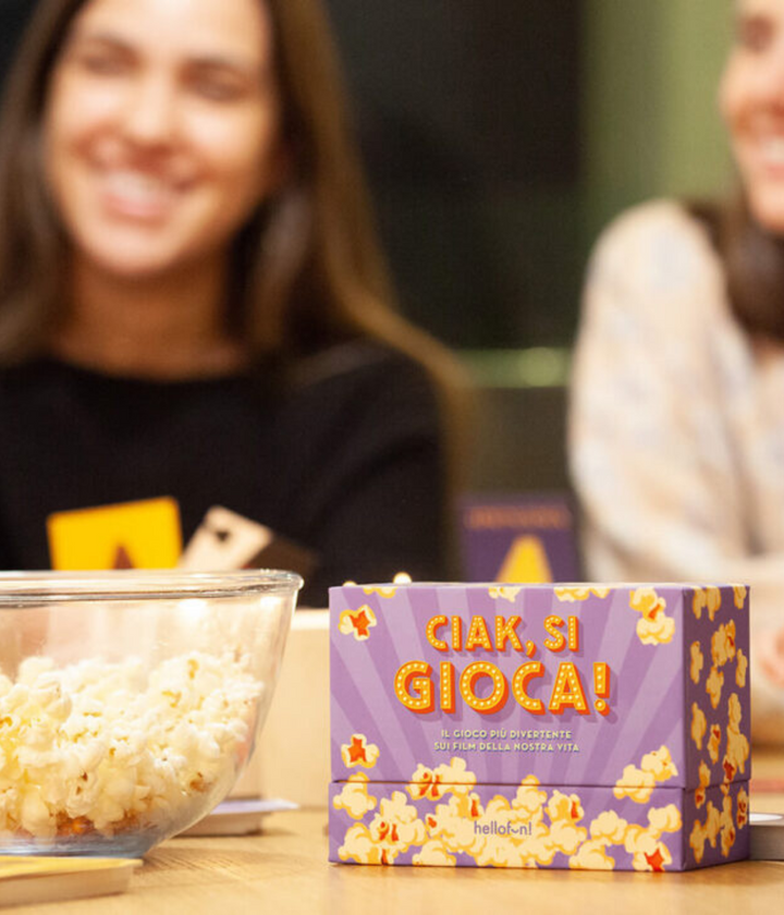 Tavolo con scatola gioco viola Ciak si gioca e ciotola con pop corn. sfondo persone che giocano.