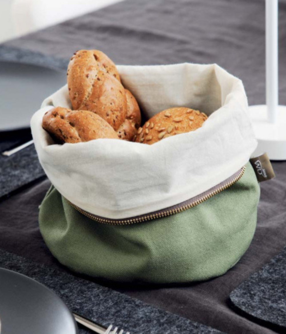 Un sacchetto portapane verde e bianco con cerniera e pane dentro. Sfondo tavola con tovaglia grigia.