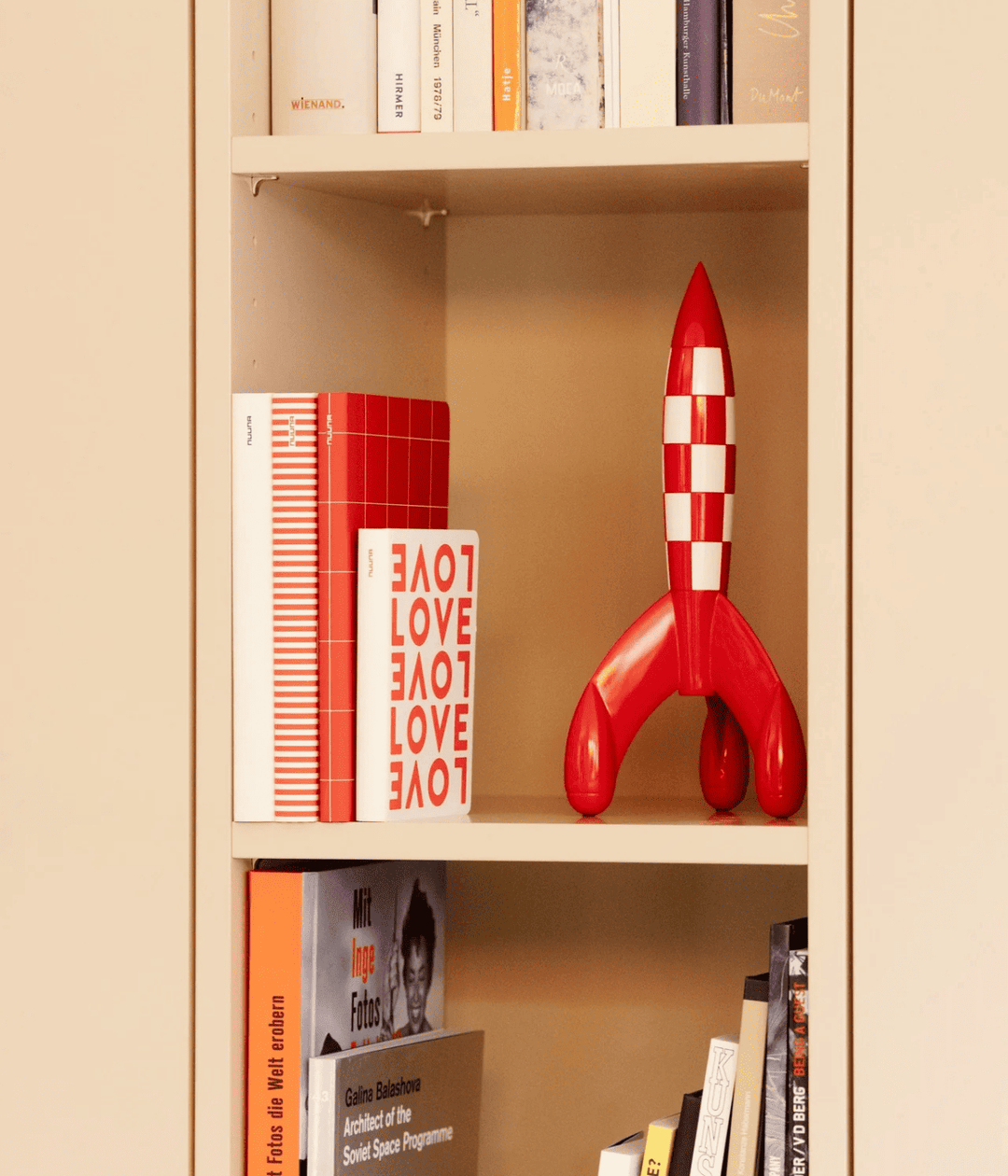 Libreria bianca con libri e Notebook bianco, con scritta love rossa, esposti. Razzo bianco e rosso.